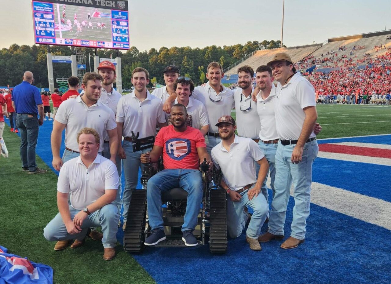 Veteran in track chair with young men on football field