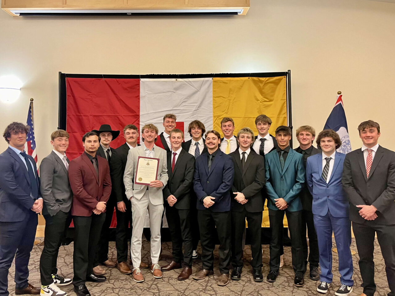 group of men in suits in front of large KA flag