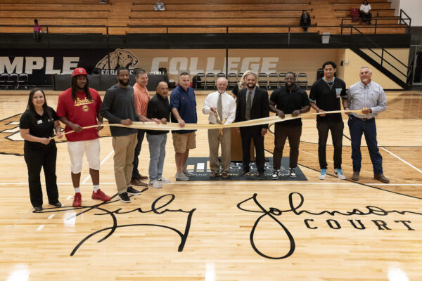 people standing on basketball court with Kirby Johnson's signature on floor with ribbon and large scissors