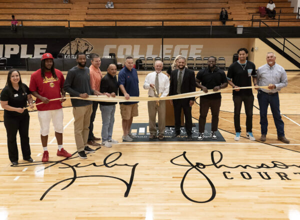 people standing on basketball court with Kirby Johnson's signature on floor with ribbon and large scissors