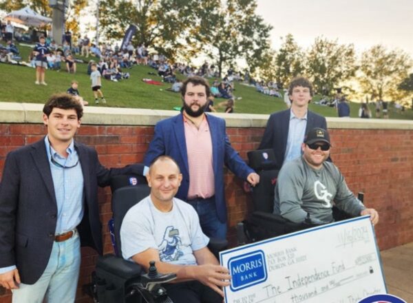 two young men standing with two veterans in track wheel chairs holding large donation check