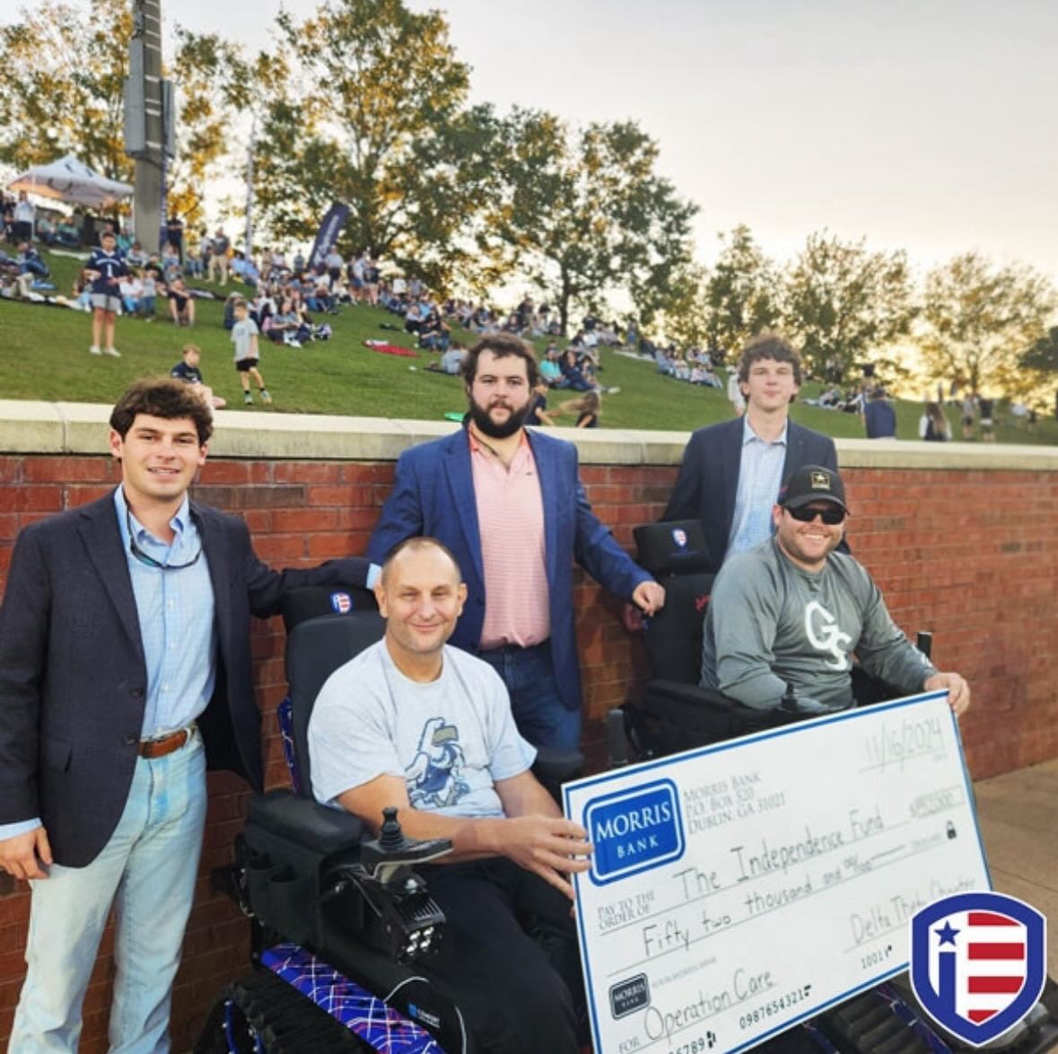 two young men standing with two veterans in track wheel chairs holding large donation check