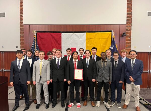 group of young men in suits in front of large KA flag holding certificate