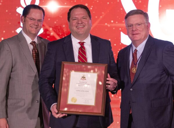 three men in suits with center holding framed certificate