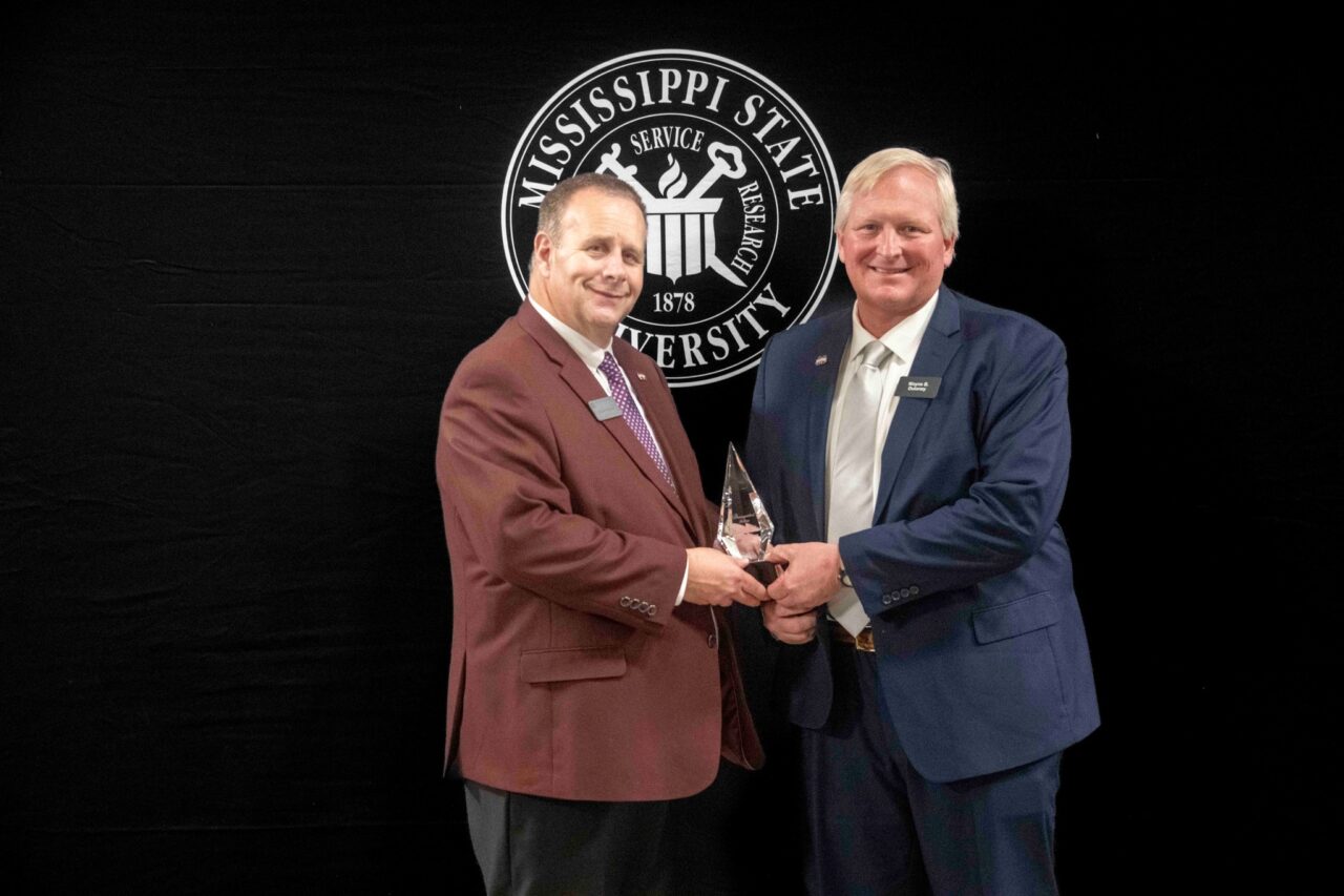 man in suit presenting award to another man in a suit