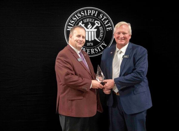 man in suit presenting award to another man in a suit